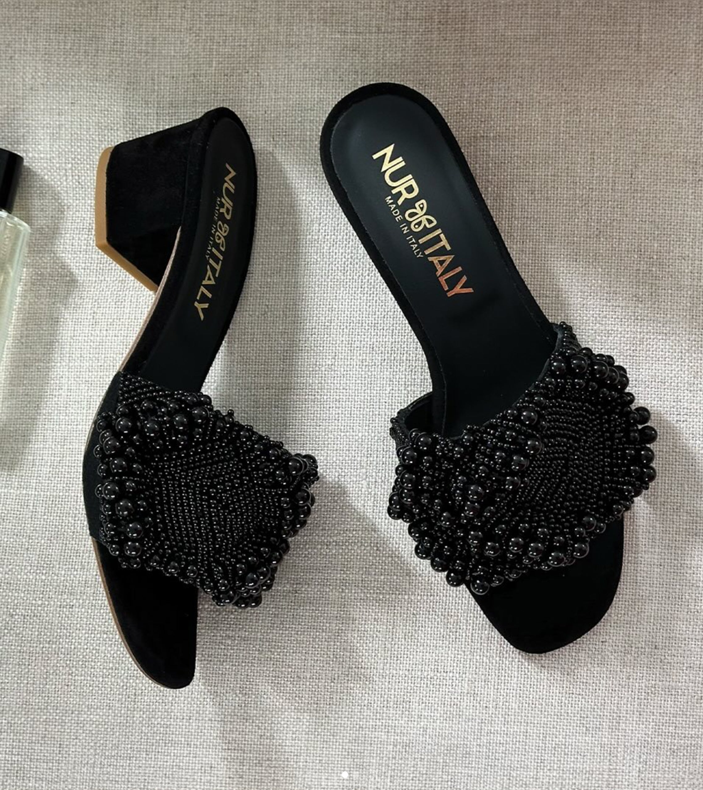 Black suede shoes with beaded embellishments on a textured surface, branded 'Nur Italy'. #color_milano black