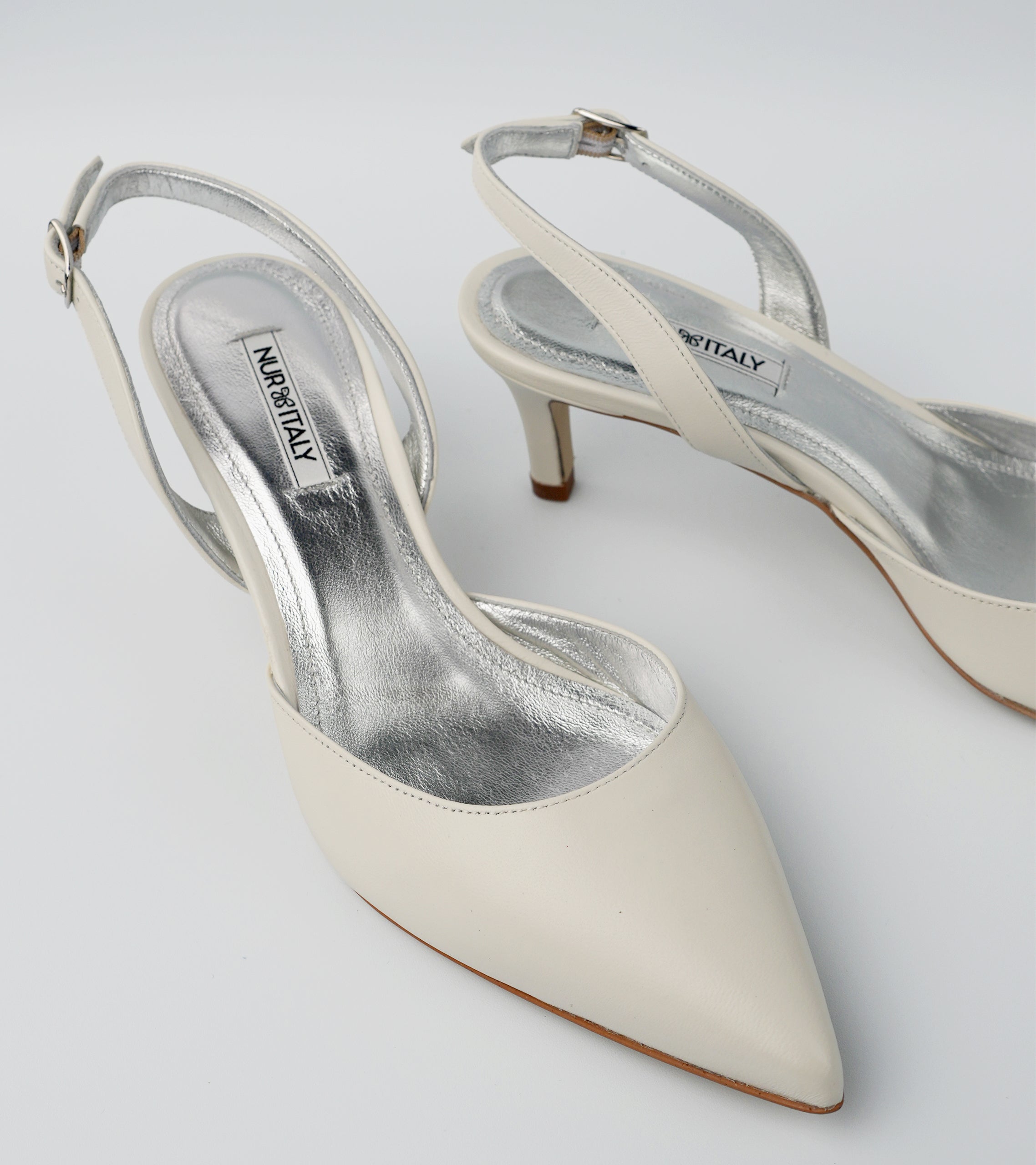 Pair of white high-heeled shoes with 'Nina Ricci' branding on a light gray background #color_amalfi white