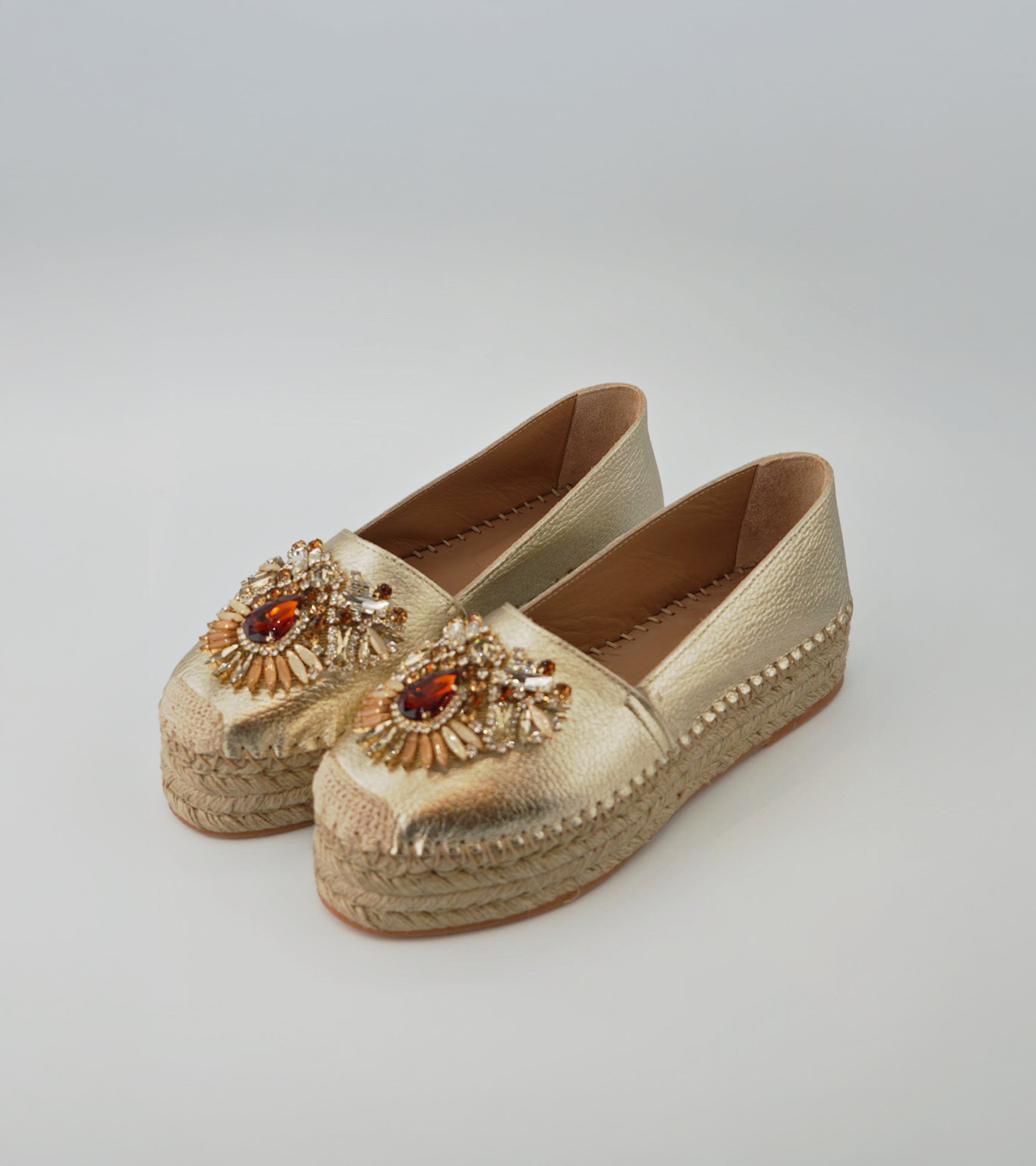 Pair of gold espadrille shoes with embellishments on a light gray background #color_venezia gold