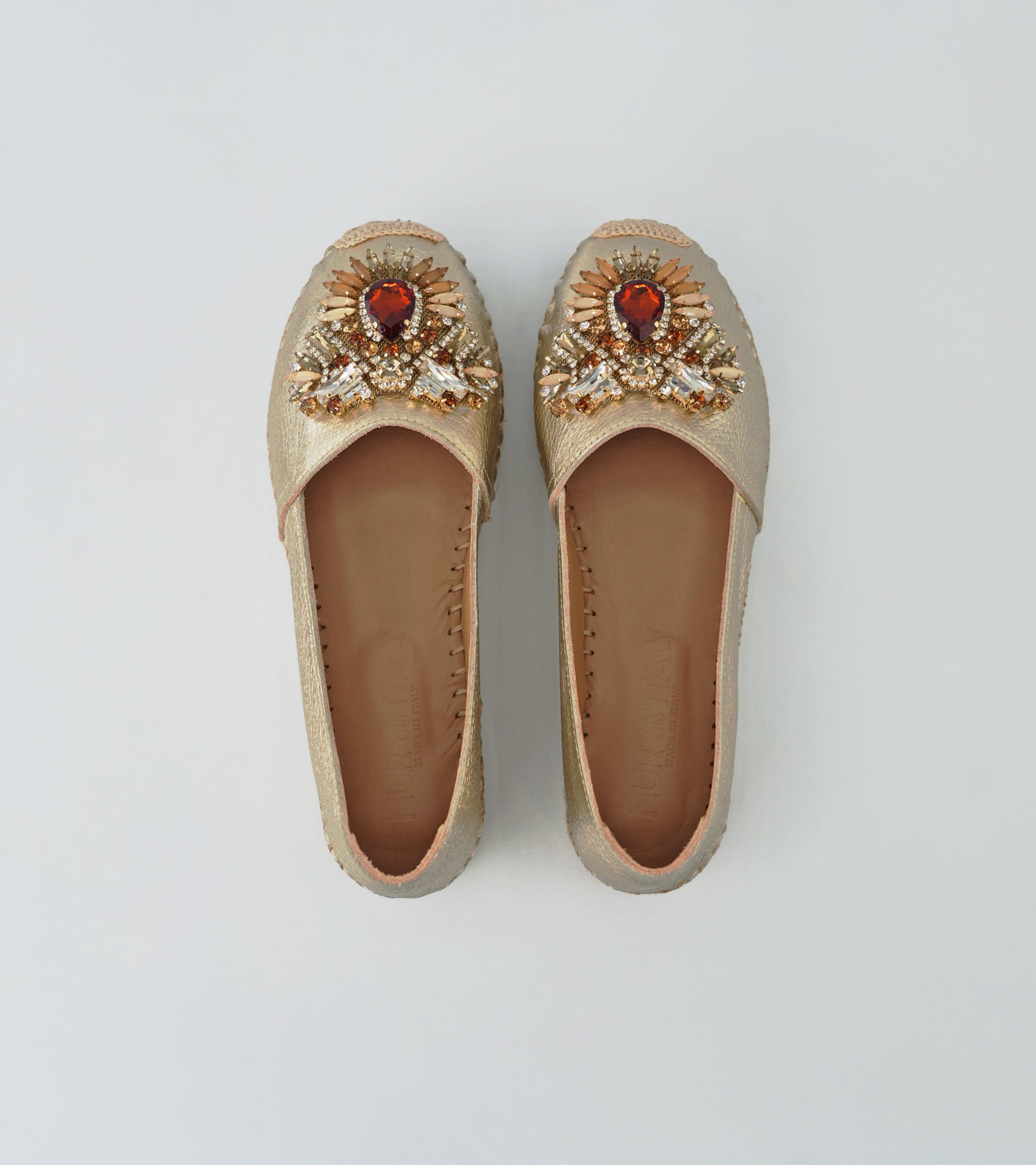 Pair of gold embellished shoes with red stones on a light gray background #color_venezia gold