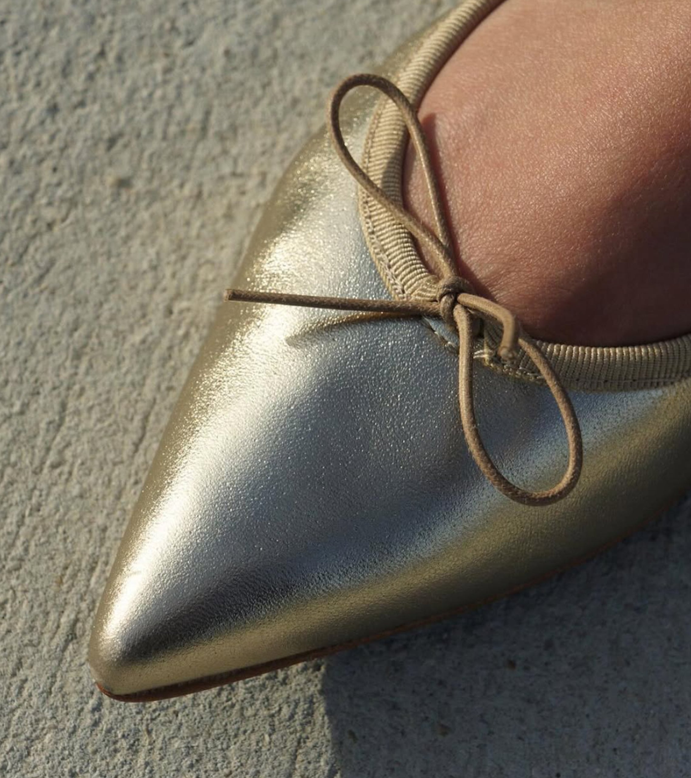 Gold metallic pointed-toe shoe with a lace-up design on a concrete surface #color_venezia gold