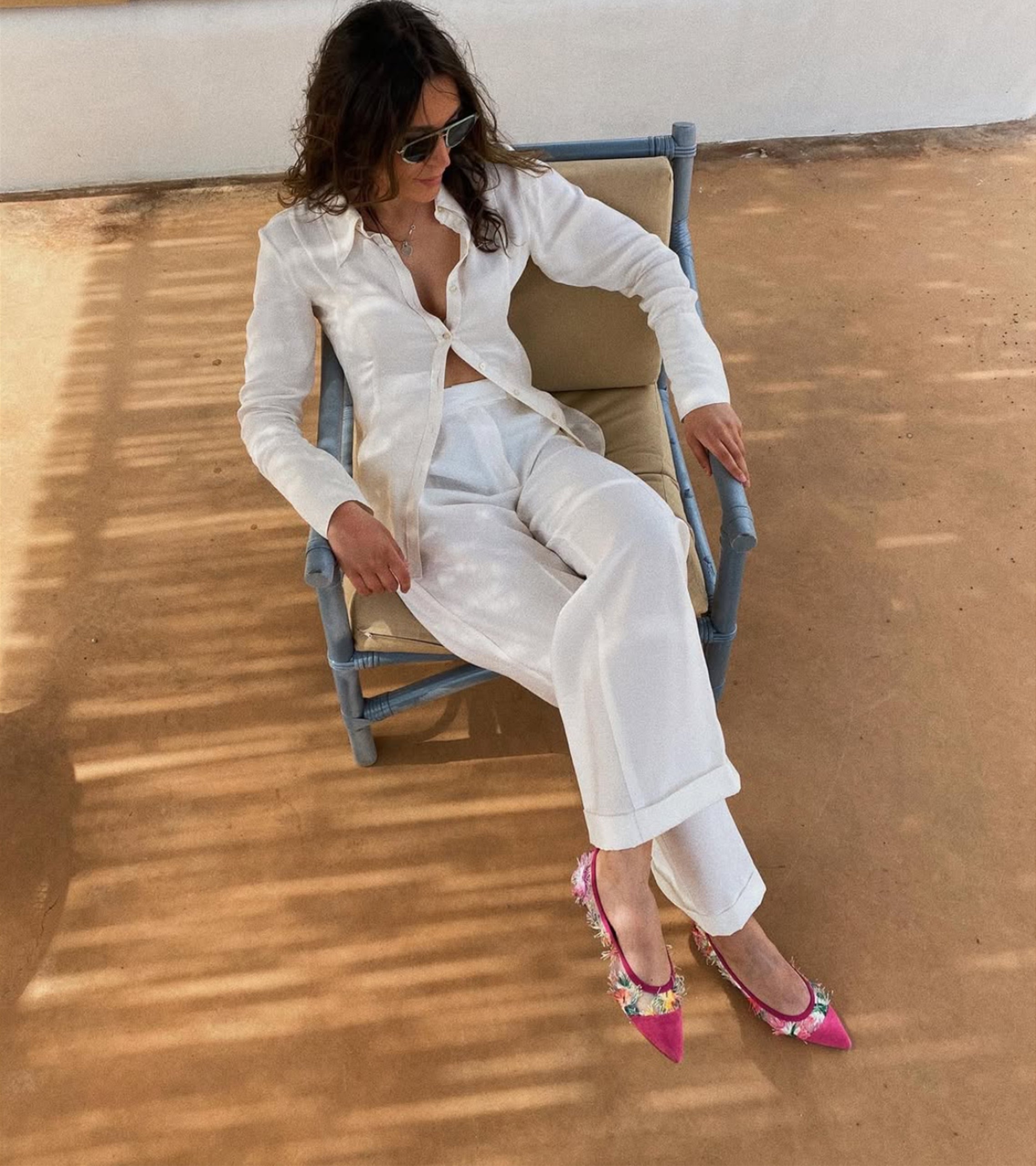 Woman in white outfit with colorful shoes sitting on a chair outdoors. #color_bari fuchsia
