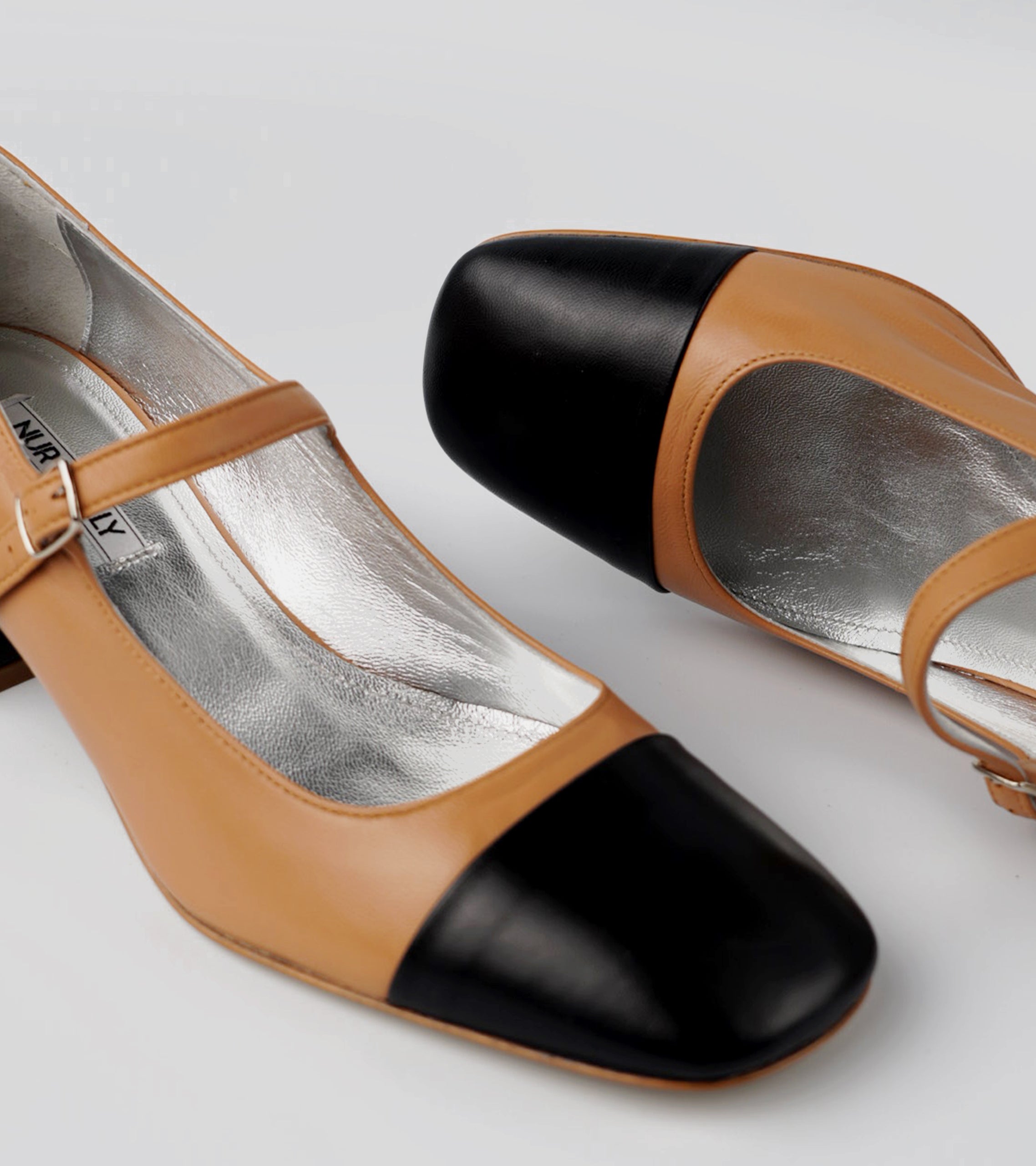 Pair of high-heeled shoes with black and tan design on a light gray background #color_palermo tan milano black