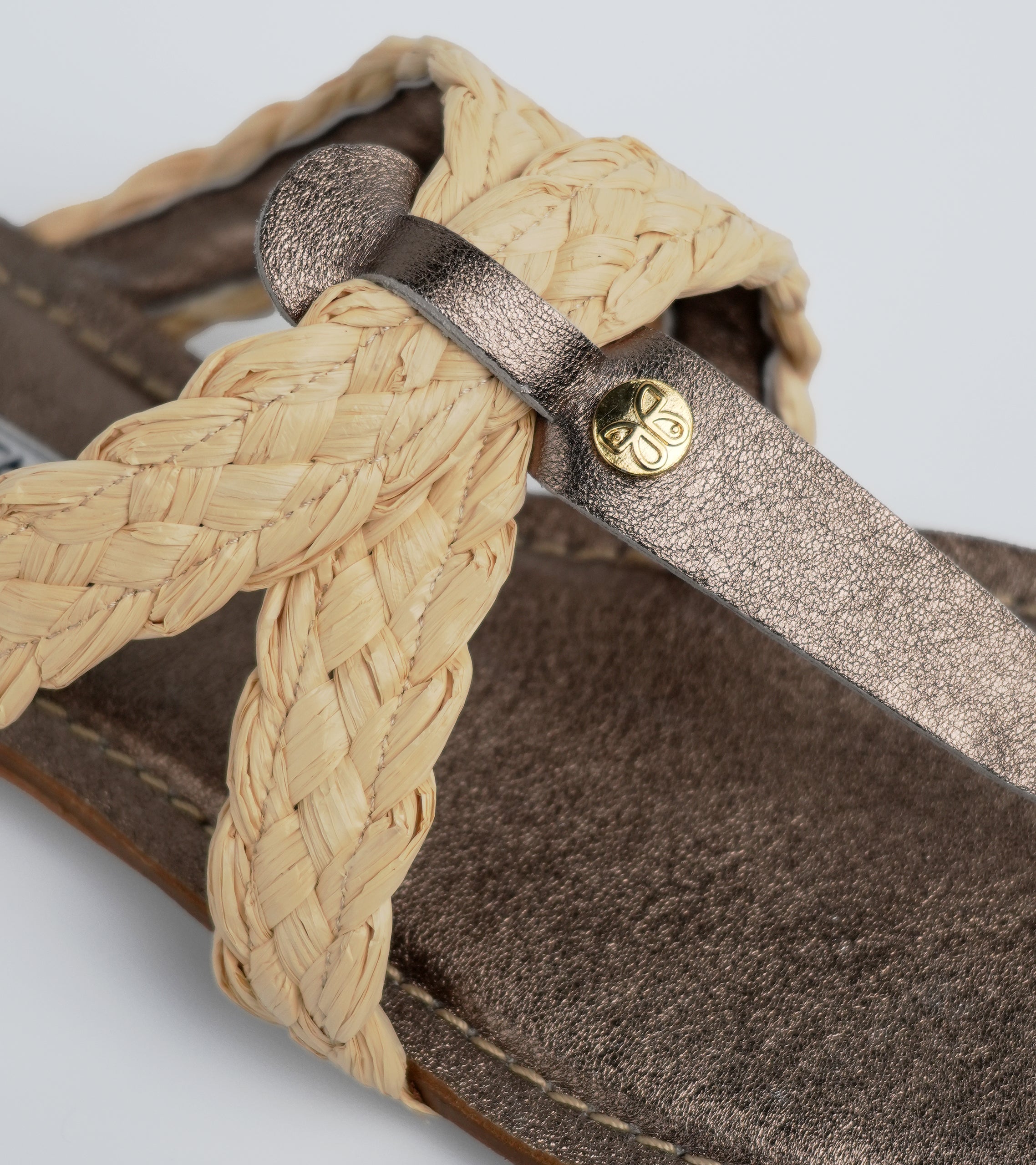 Close-up of a sandal with woven strap and gold buckle on a light gray background #color_siena bronze