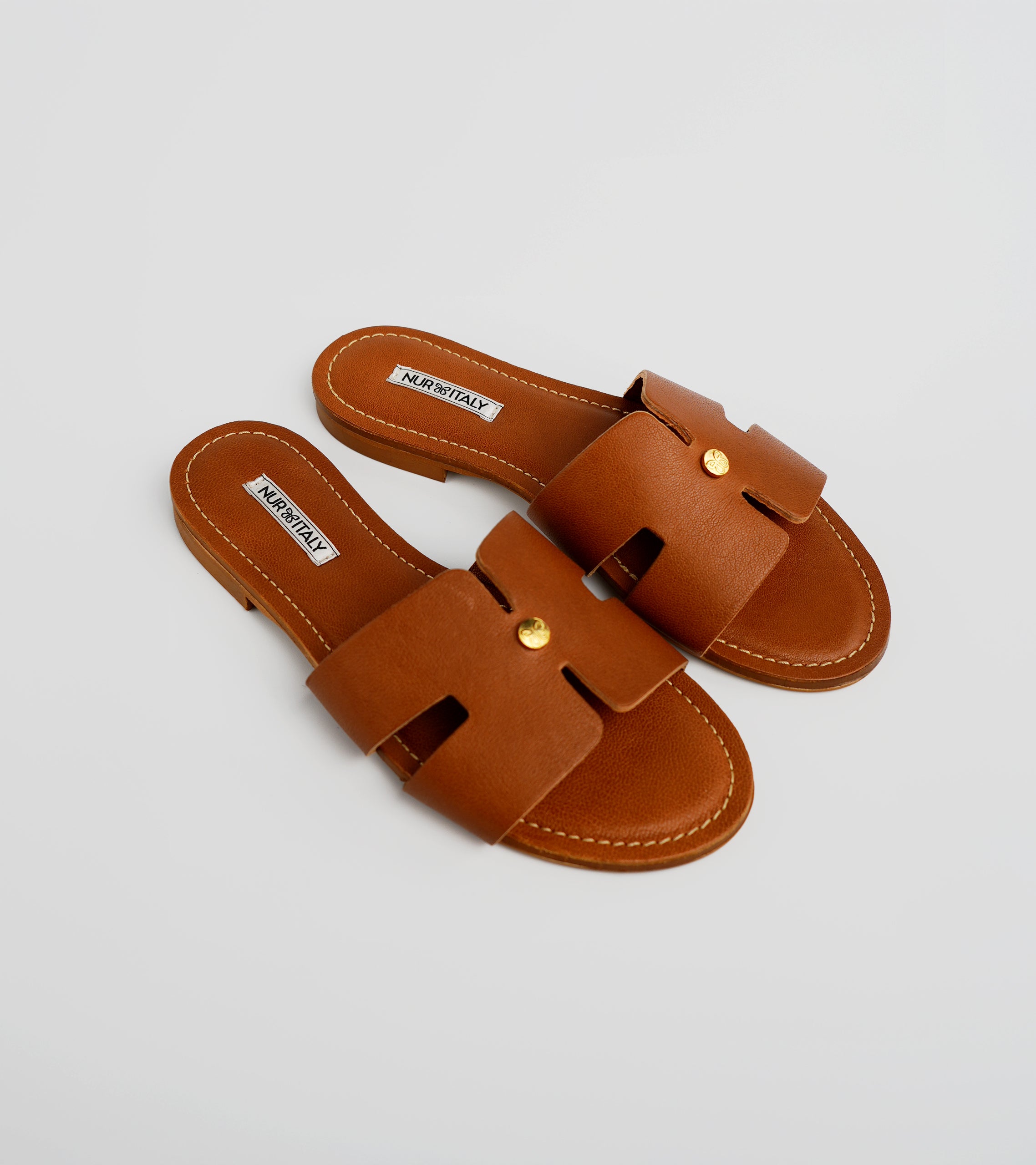 Pair of brown sandals with gold accents on a light gray background #color_palermo tan