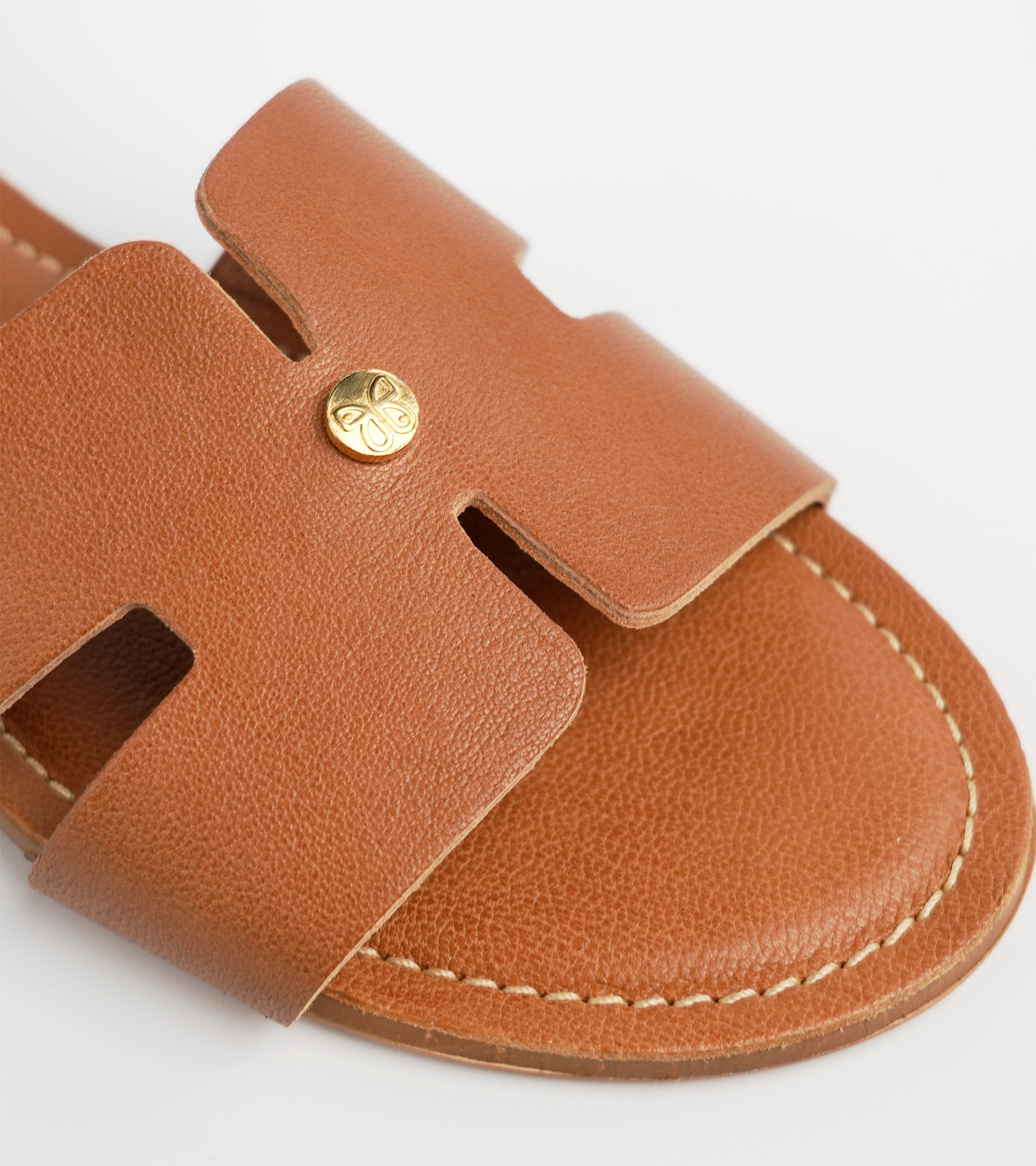 Brown sandal with a gold button on a white background #color_palermo tan