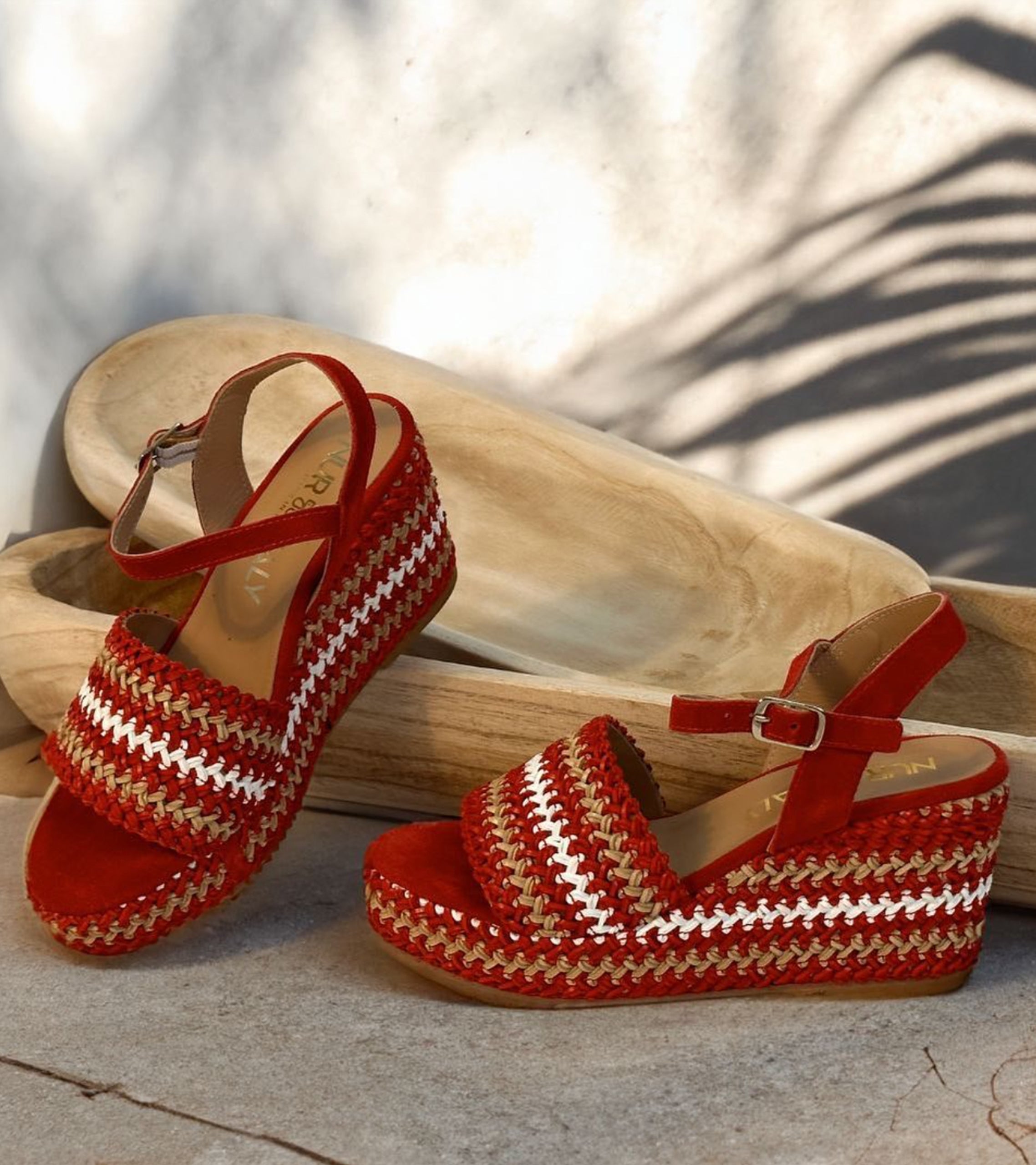 Red and white woven sandals on a stone surface with a blurred natural background