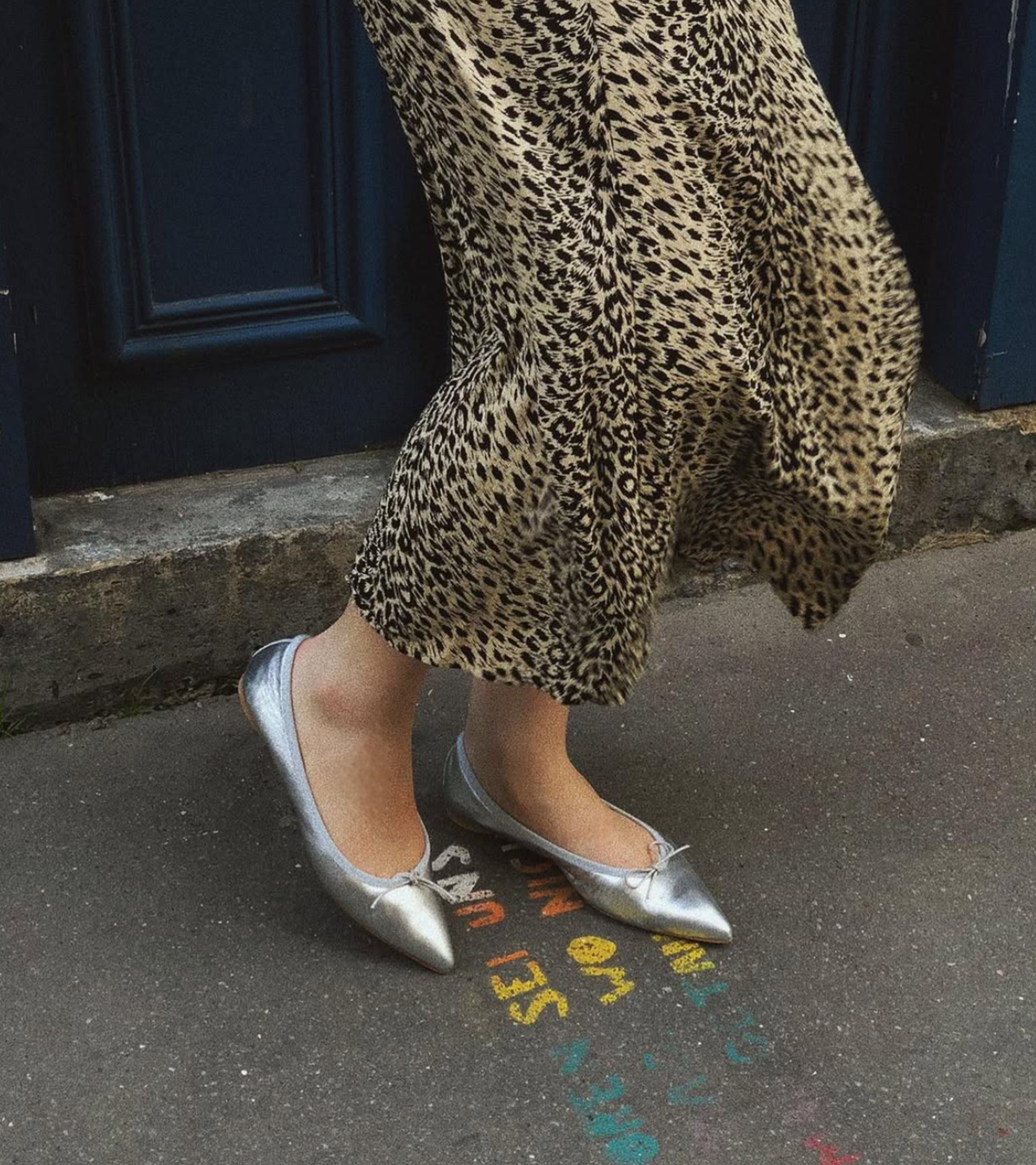 Person wearing leopard print pants and silver flats on a sidewalk. #color_napoli silver