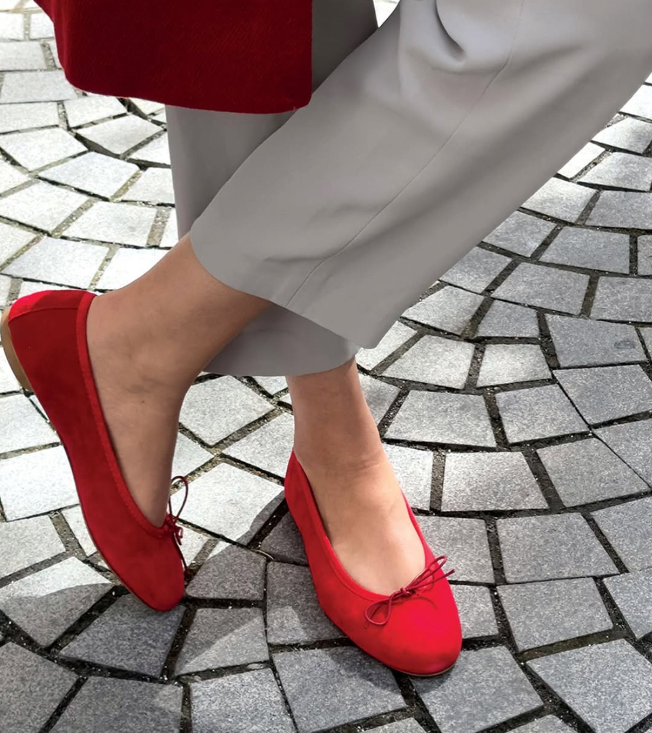Red suede shoes worn on a stone pavement #color_varese fire