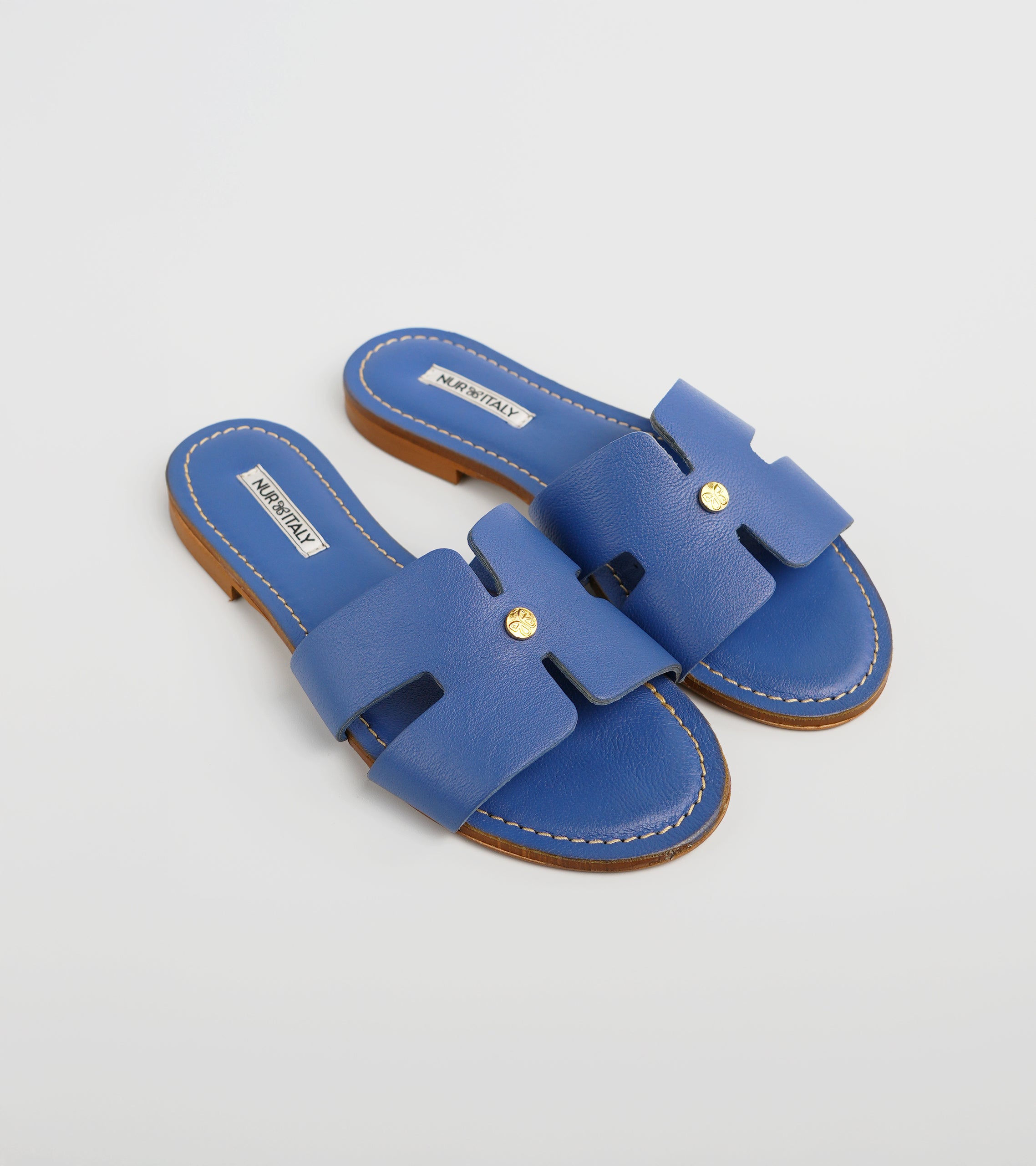 Pair of blue sandals with a gold buckle on a light gray background #color_capri blue