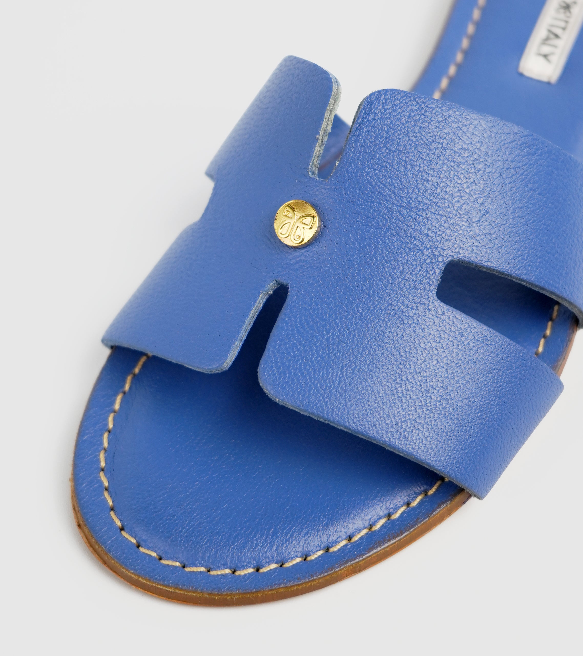 Blue sandal with a gold button on a light gray background #color_capri blue