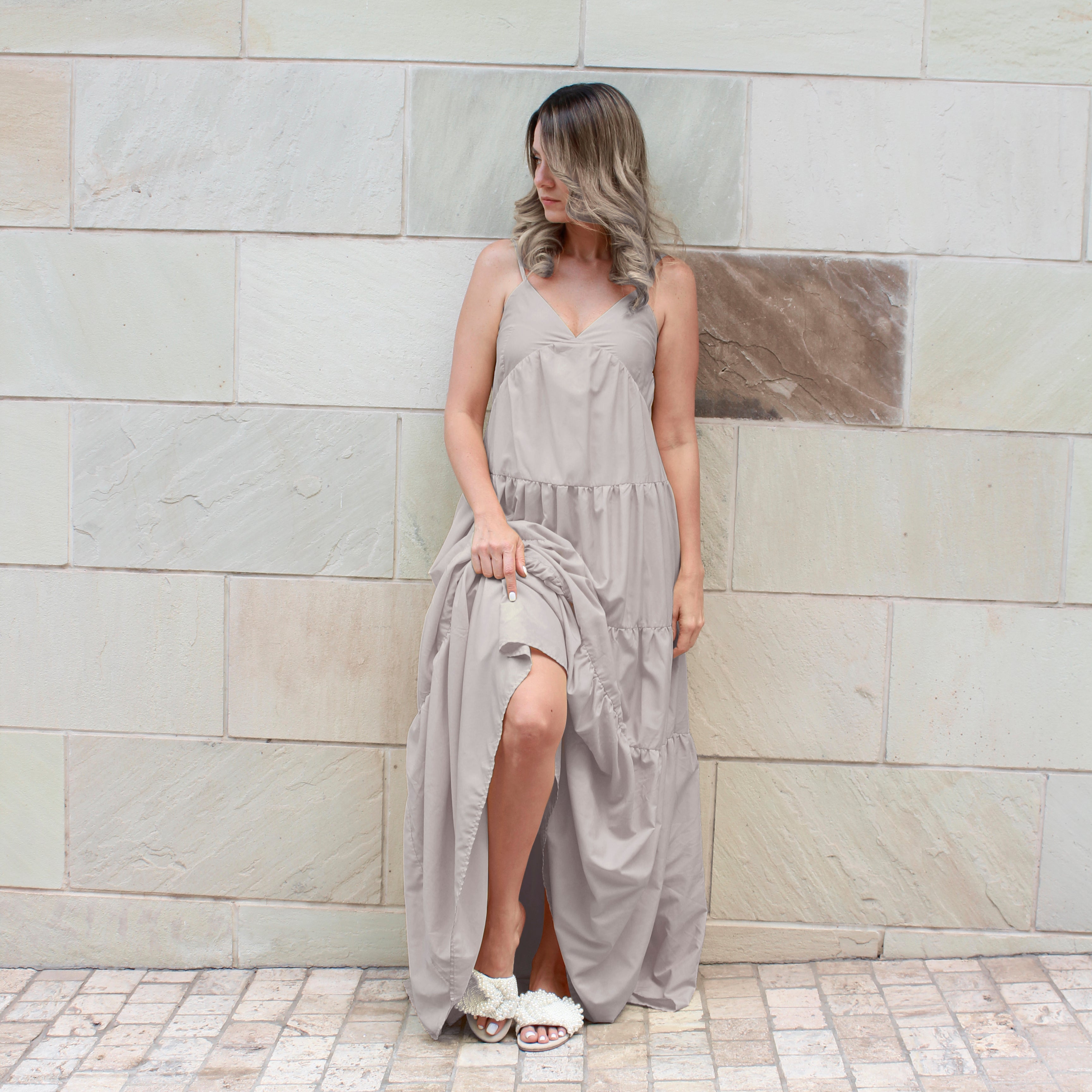 Woman on a cream long dress, sticking out a leg showing her white pearl flat sandals